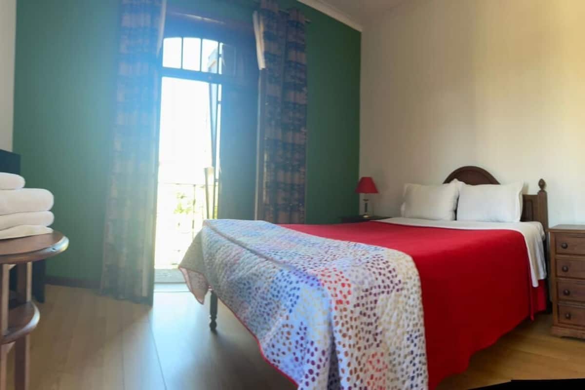 A bedroom with a bed, a nightstand, a lamp, and a window with curtains.