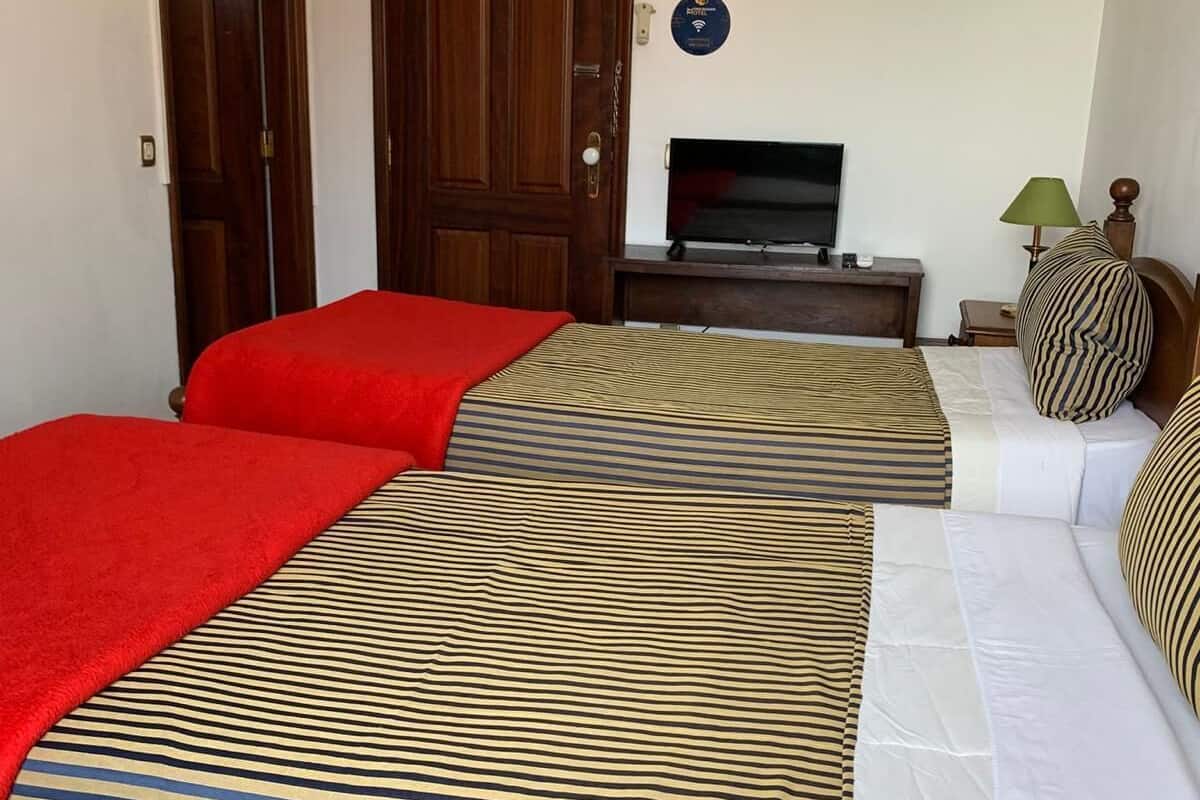 A hotel room with two beds, a TV, a lamp, and a door.