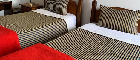 A hotel room with two beds, each with striped bedding and a red blanket. There is a nightstand with a lamp and a telephone.