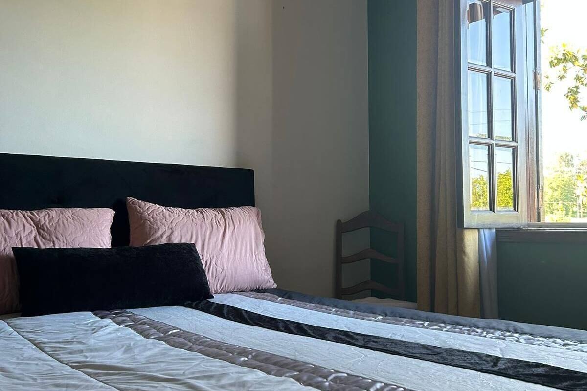 A bedroom with a large bed, a headboard, and a window with curtains.