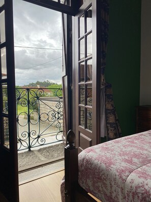 Een kamer met een bed, een balkon met een ijzeren hekwerk en uitzicht op de omgeving.