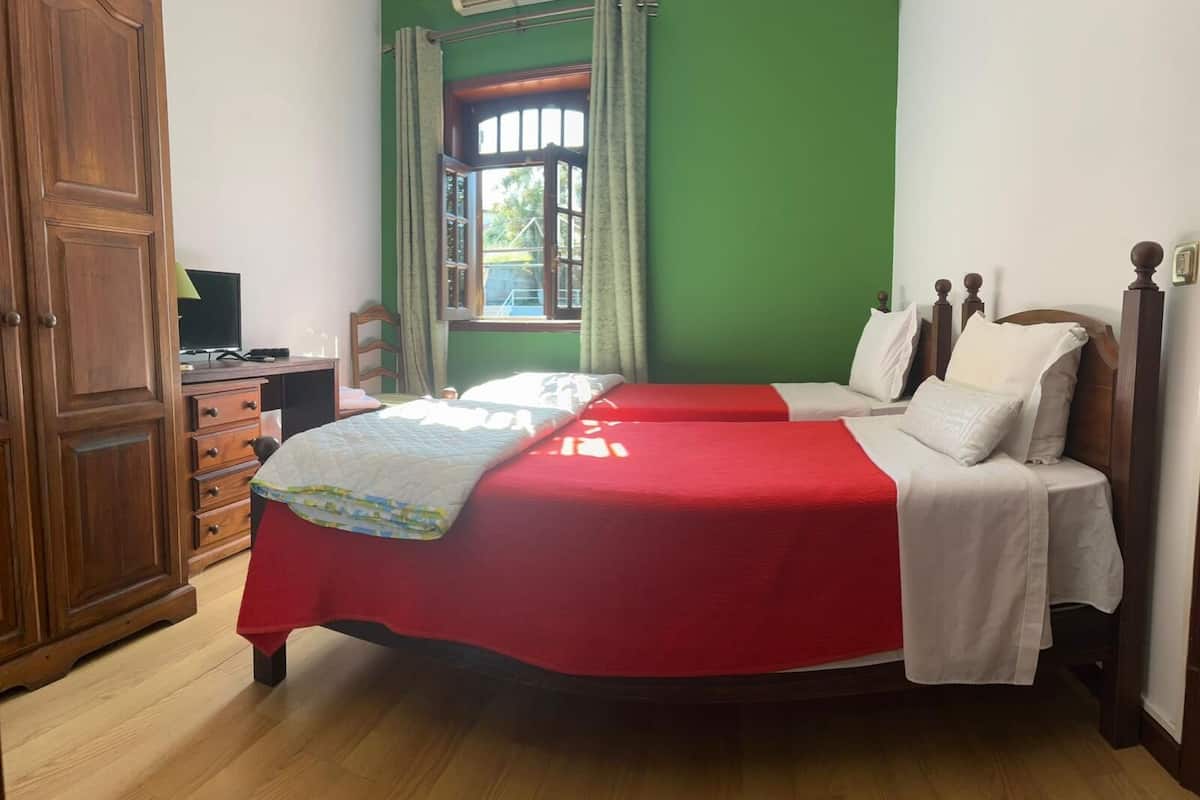 A room with two beds, a wooden wardrobe, a desk with a computer, and a window with curtains.
