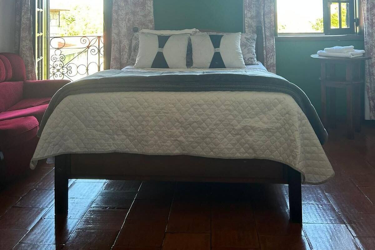 A bedroom with a bed, curtains, an air conditioning unit, and a view of the outdoors.