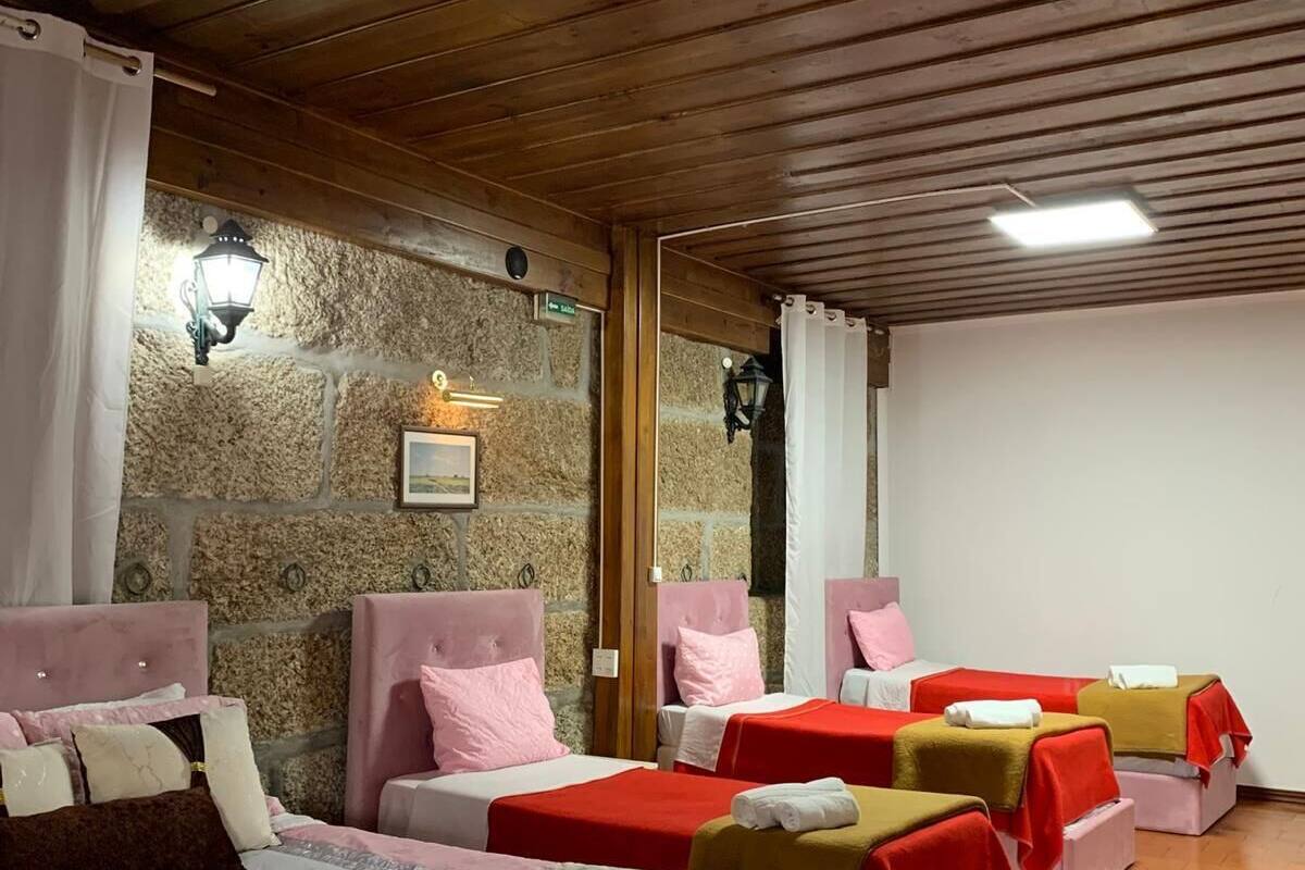 A hotel room with four beds, stone walls, wooden ceiling beams, and a stone fireplace.