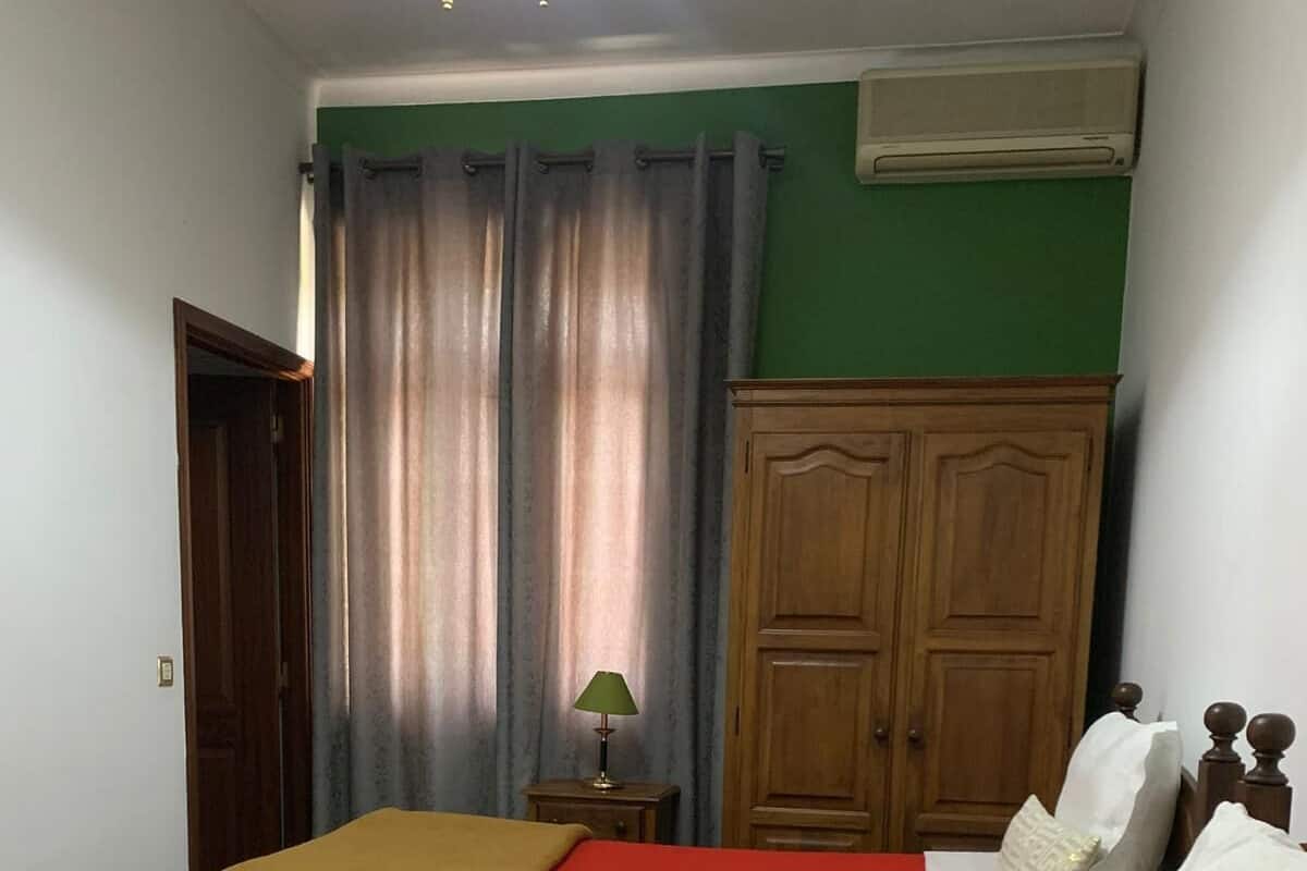 A room with two beds, a wooden wardrobe, a green wall, and a window with curtains.