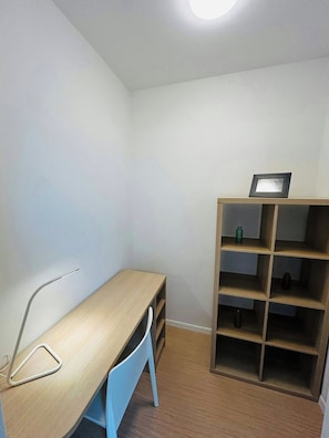 A small, well-lit room with a wooden desk, a chair, and a built-in bookshelf.