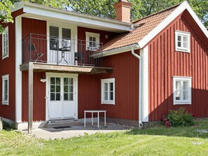 Una casa de madera roja de dos pisos, con un balcón, puertas y ventanas blancas.