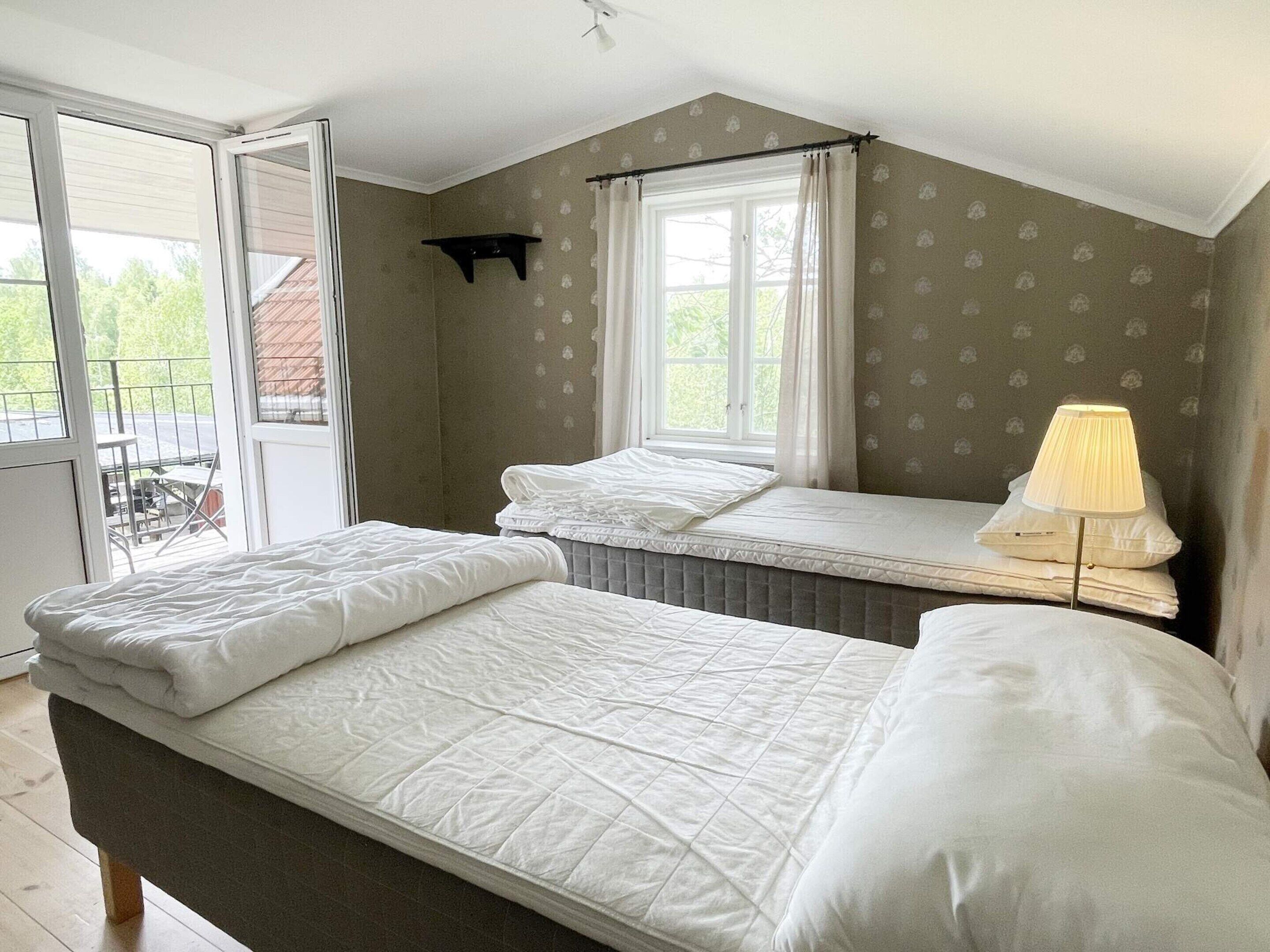 Un dormitorio con una cama, una ventana con cortinas, un estante pequeño y una lámpara.
