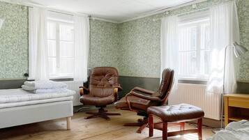 A room with a bed, two leather armchairs, a desk, and a lamp.