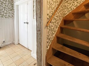 Una habitación con una escalera de madera, una puerta blanca y papel tapiz estampado.