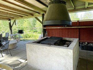 Zona de parrilla exterior con chimenea, asientos de hormigón y vistas a zonas verdes.