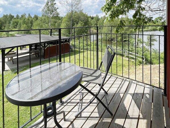 Un balcón con una mesa y sillas de vidrio, con vista a un área verde con una mesa de picnic y un edificio al fondo.