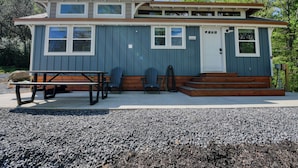 A two-story house with a front porch, a table, and two Adirondack chairs.