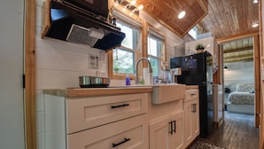 A compact kitchen with white cabinets, a black refrigerator, and a window providing natural light.