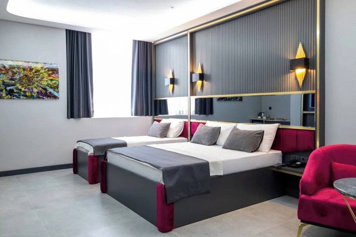 Una habitación de hotel moderna con dos camas, un espejo grande y un sillón rojo.