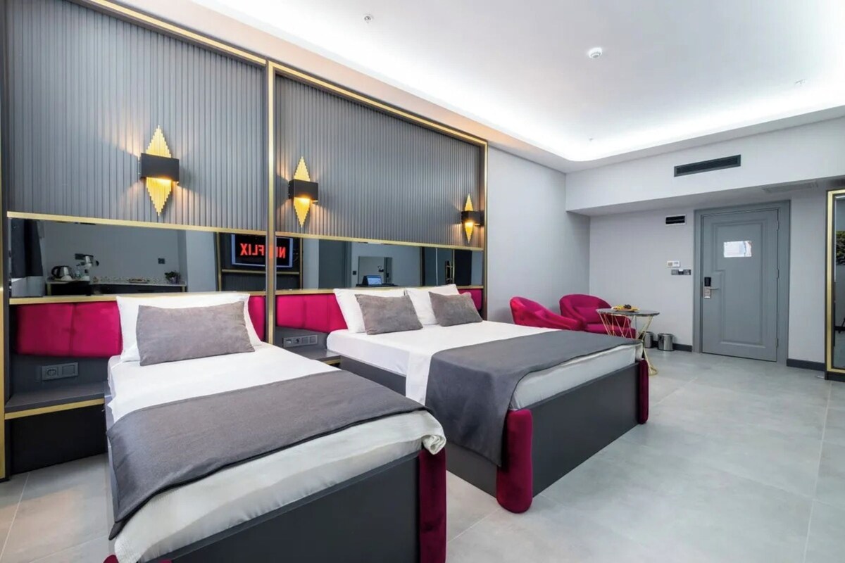 A modern hotel room with two beds, a large mirror, and a red chair.