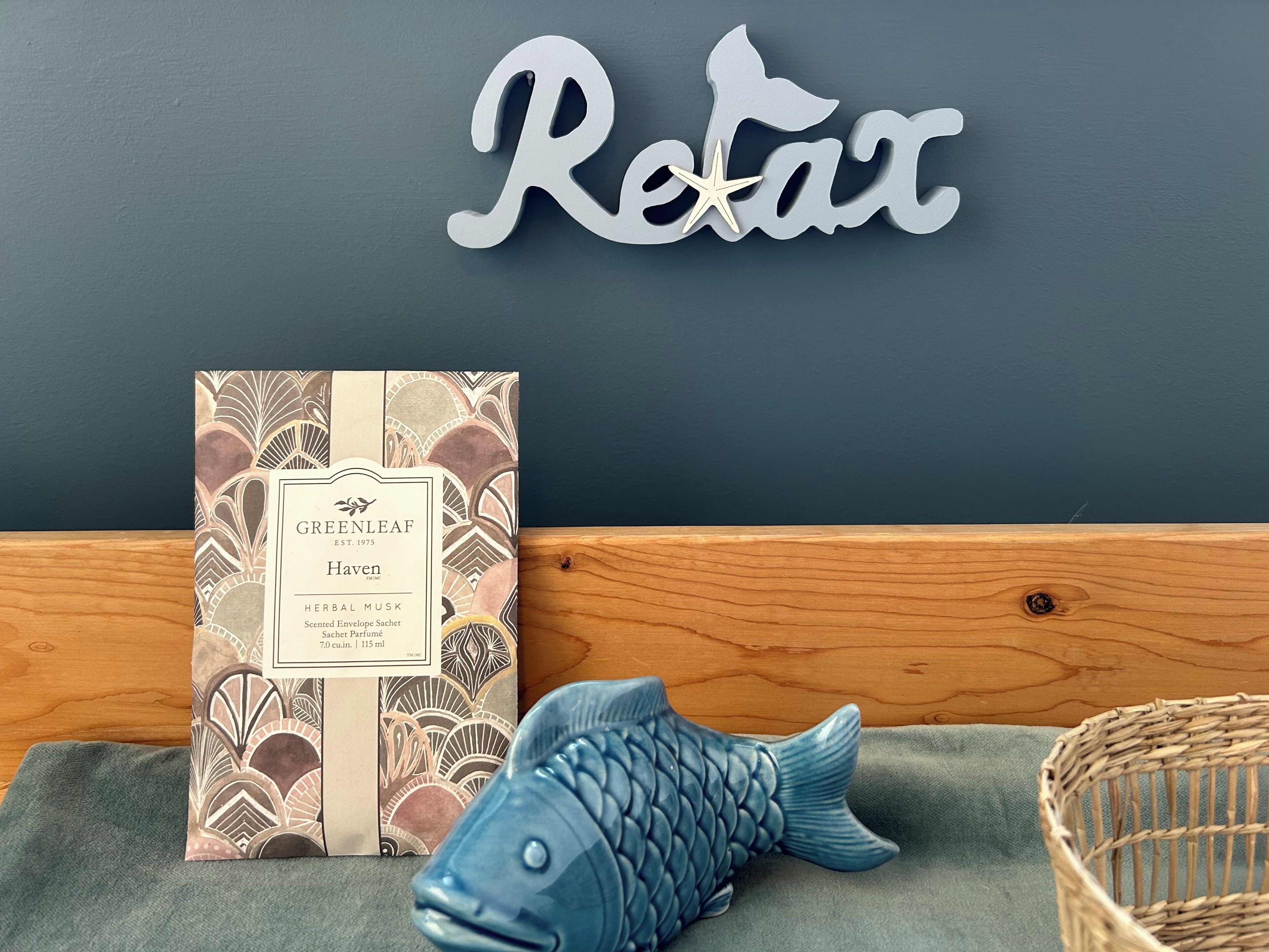 A package of Greenleaf Haven Herbal Musk, a blue fish-shaped decorative item, and a woven basket on a wooden surface.