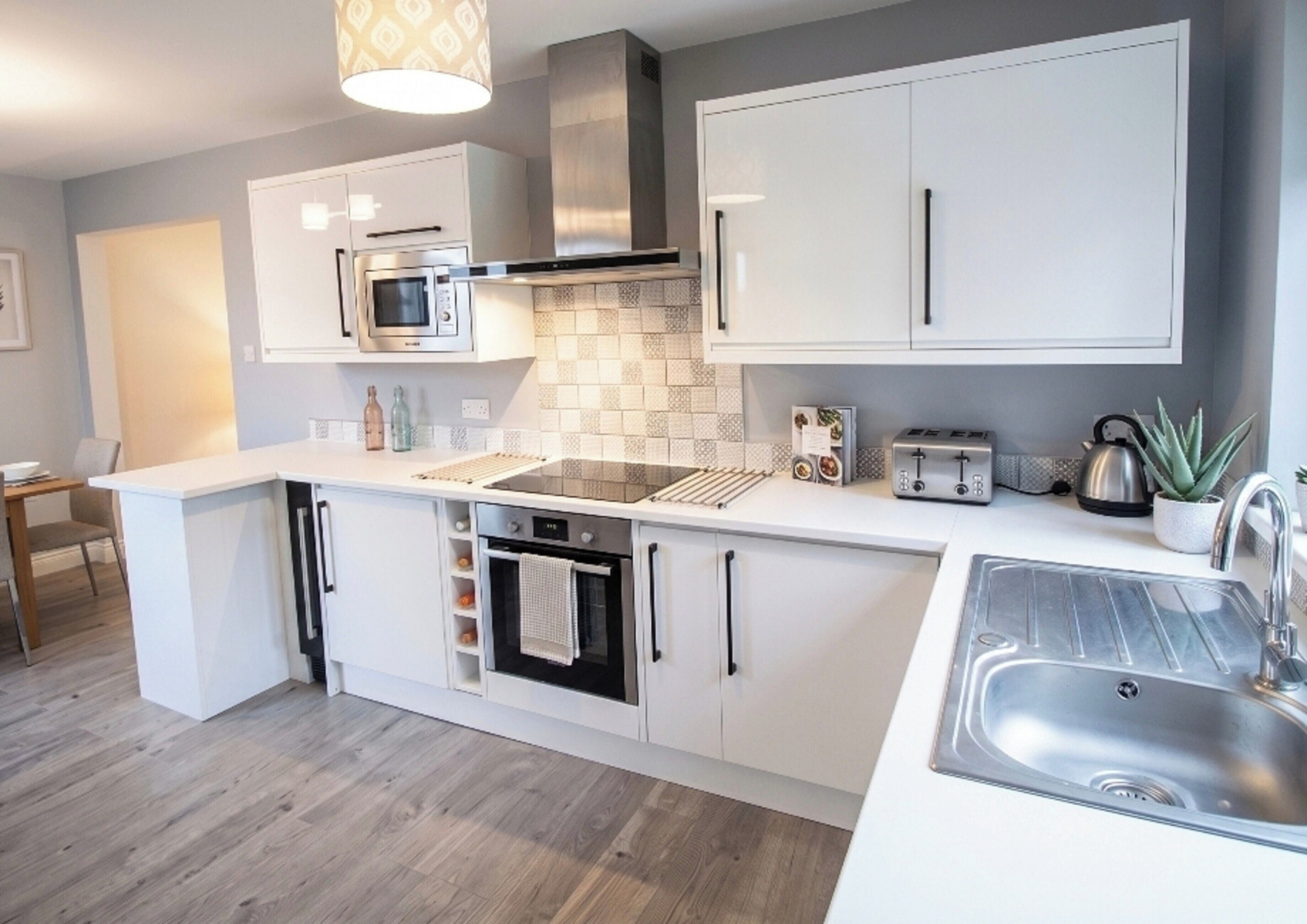 A modern kitchen with white cabinetry, a built-in oven, a microwave, a toaster, and a sink.