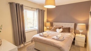 A bedroom with a bed, two bedside tables, a window with curtains, and a lamp on each table. - 3 Bed House - Sleeps 6 - Parking - Pets - Garden (Rowlands Gill)