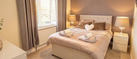 A bedroom with a bed, two bedside tables, a window with curtains, and a lamp on each table.