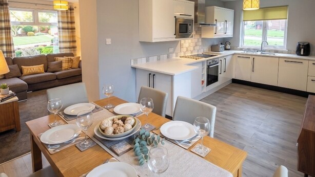 A modern kitchen with white cabinets, a central island, and a dining area set for a meal. - 3 Bed House - Sleeps 6 - Parking - Pets - Garden (Rowlands Gill)