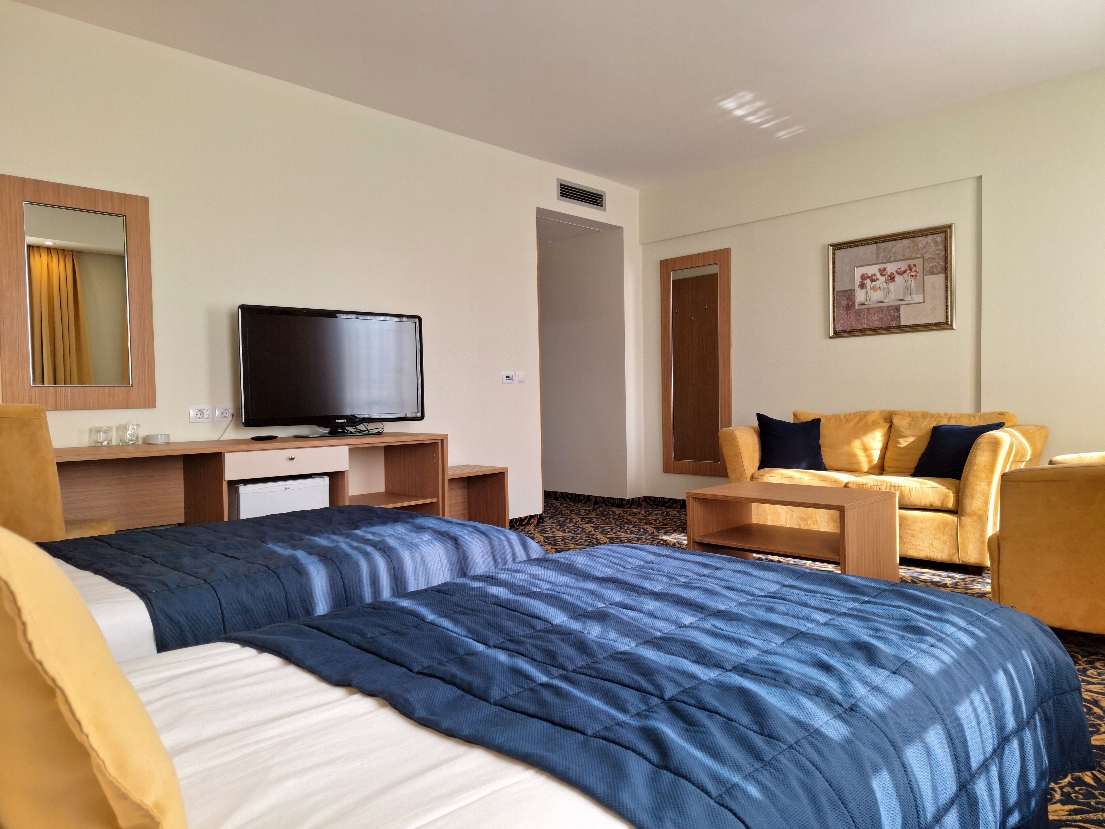 A hotel room with two beds, a television, a desk, a chair, and a sofa.