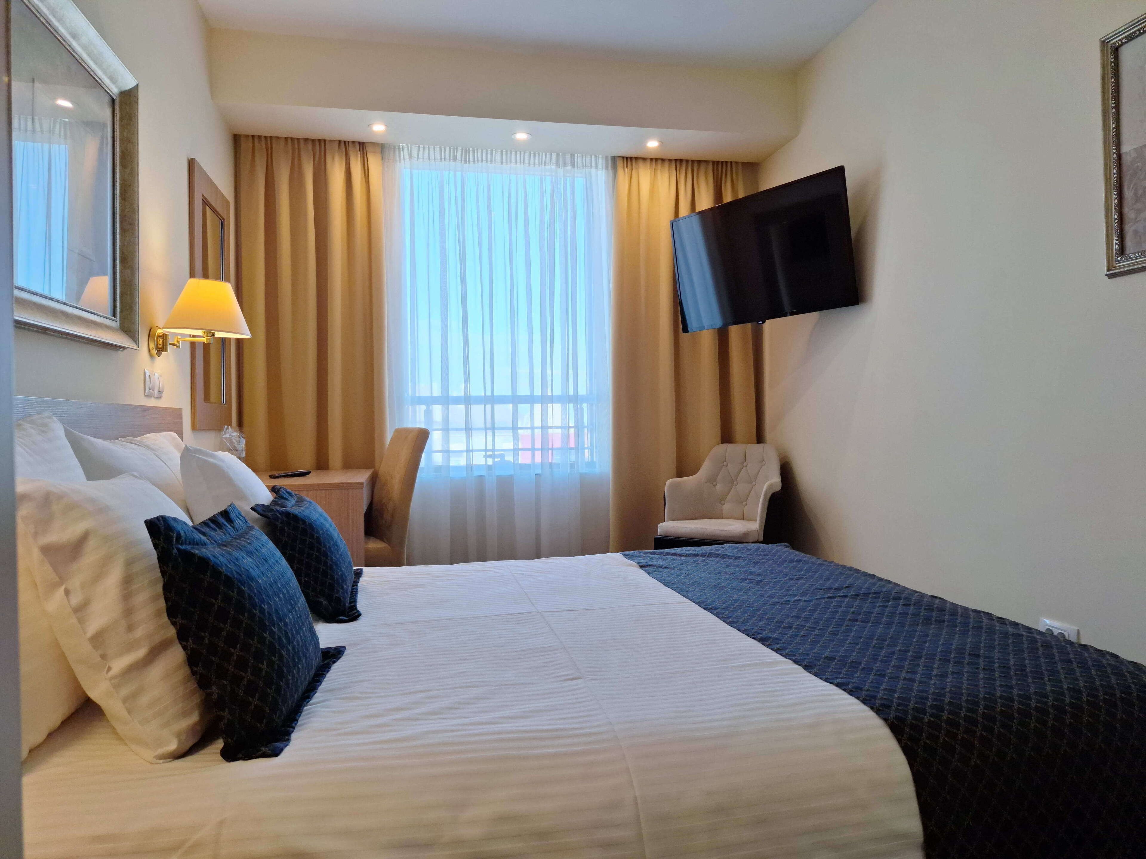 Ein Hotelzimmer mit einem großen Bett, einem Sessel, einem Schreibtisch, einem Fernseher und einem Fenster mit Vorhängen.