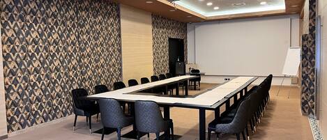 A conference room with a long table, chairs, a projector, and a whiteboard.