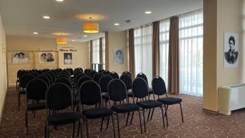Une salle de conférence avec des rangées de chaises, une moquette à motifs et de grandes fenêtres avec des rideaux.