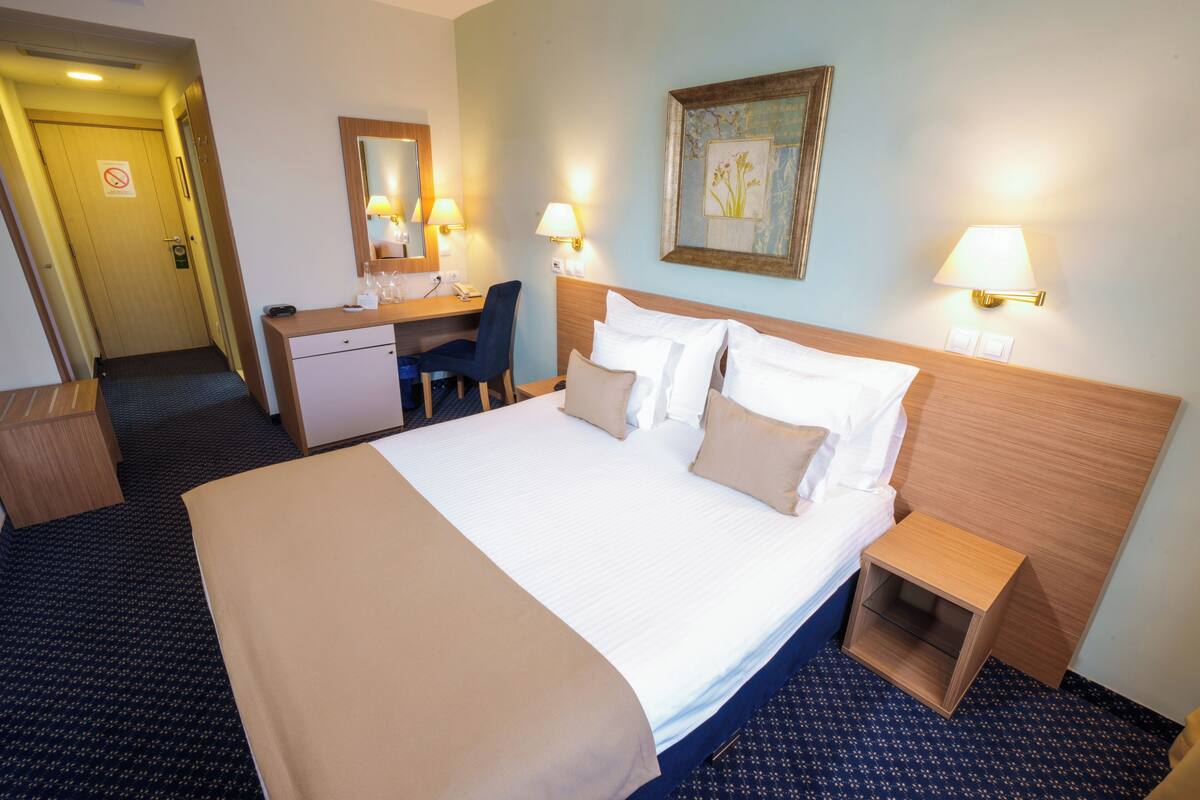A hotel room with a bed, bedside tables, a desk, a chair, and a mirror.