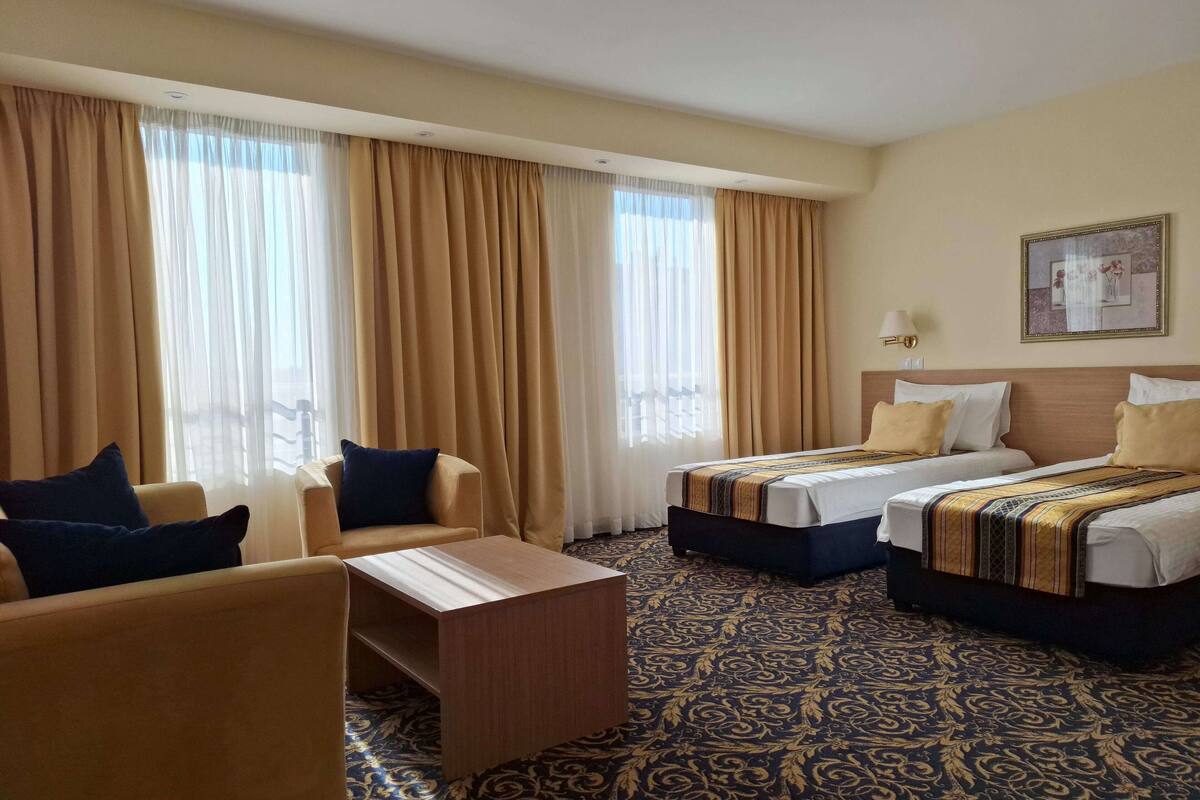 A hotel room with two beds, a sofa, a small table, and a patterned carpet.
