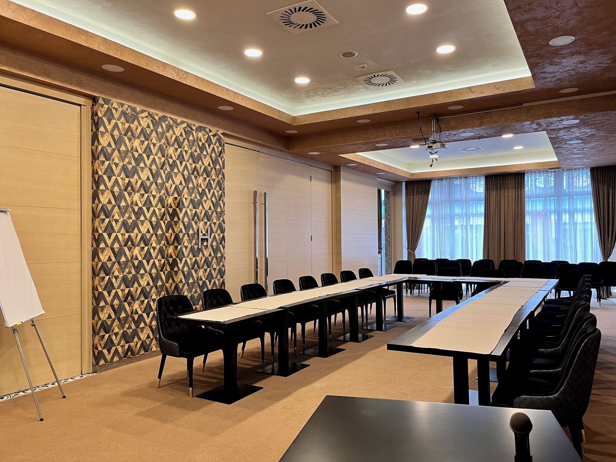 Una sala conferenze con un lungo tavolo, sedie nere, una lavagna e carta da parati decorata.