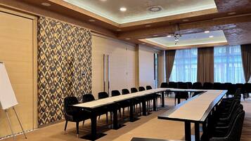 Una sala conferenze con un lungo tavolo, sedie nere, una lavagna e carta da parati decorata.