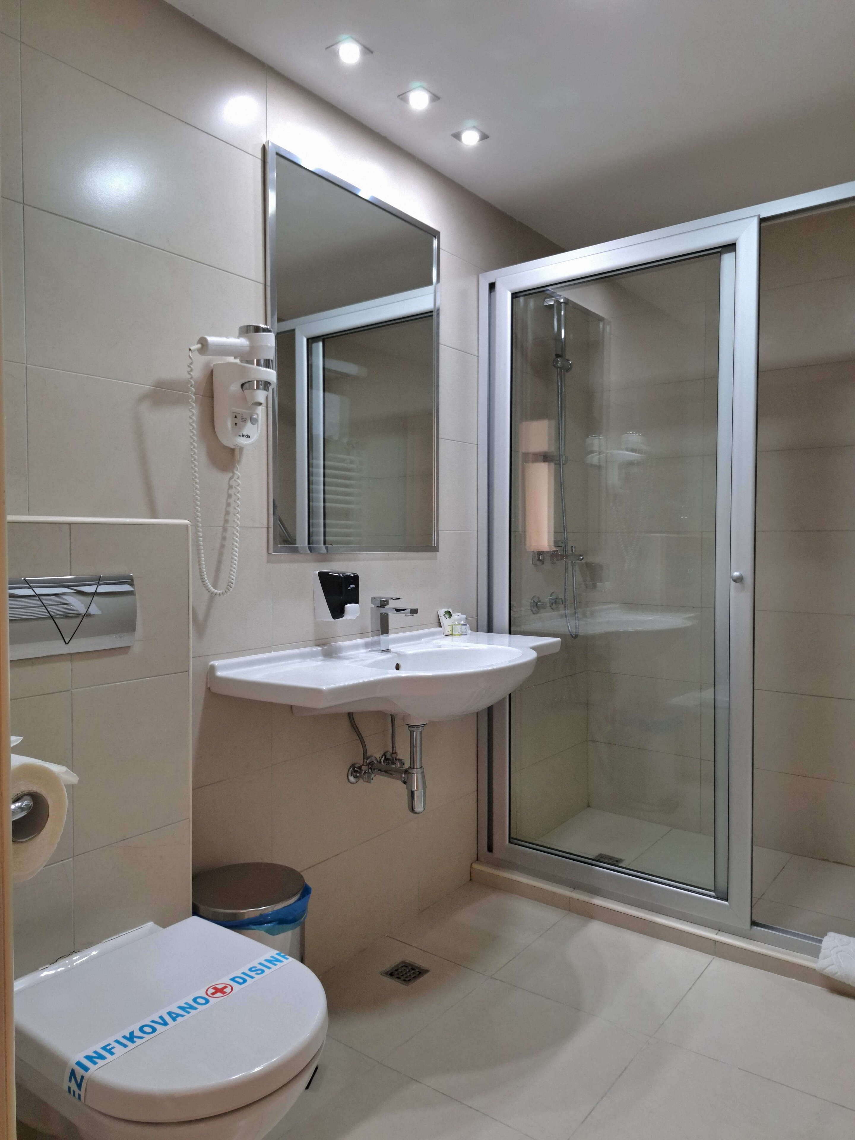 A bathroom with a toilet, sink, mirror, and glass-enclosed shower.