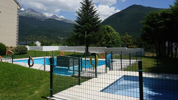 A swimming pool area with a net fence, lifebuoys, and a mountain backdrop.