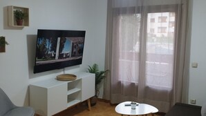 A living room with a flat-screen TV, a white entertainment unit, a grey sofa, a small white table, and a ceiling fan.