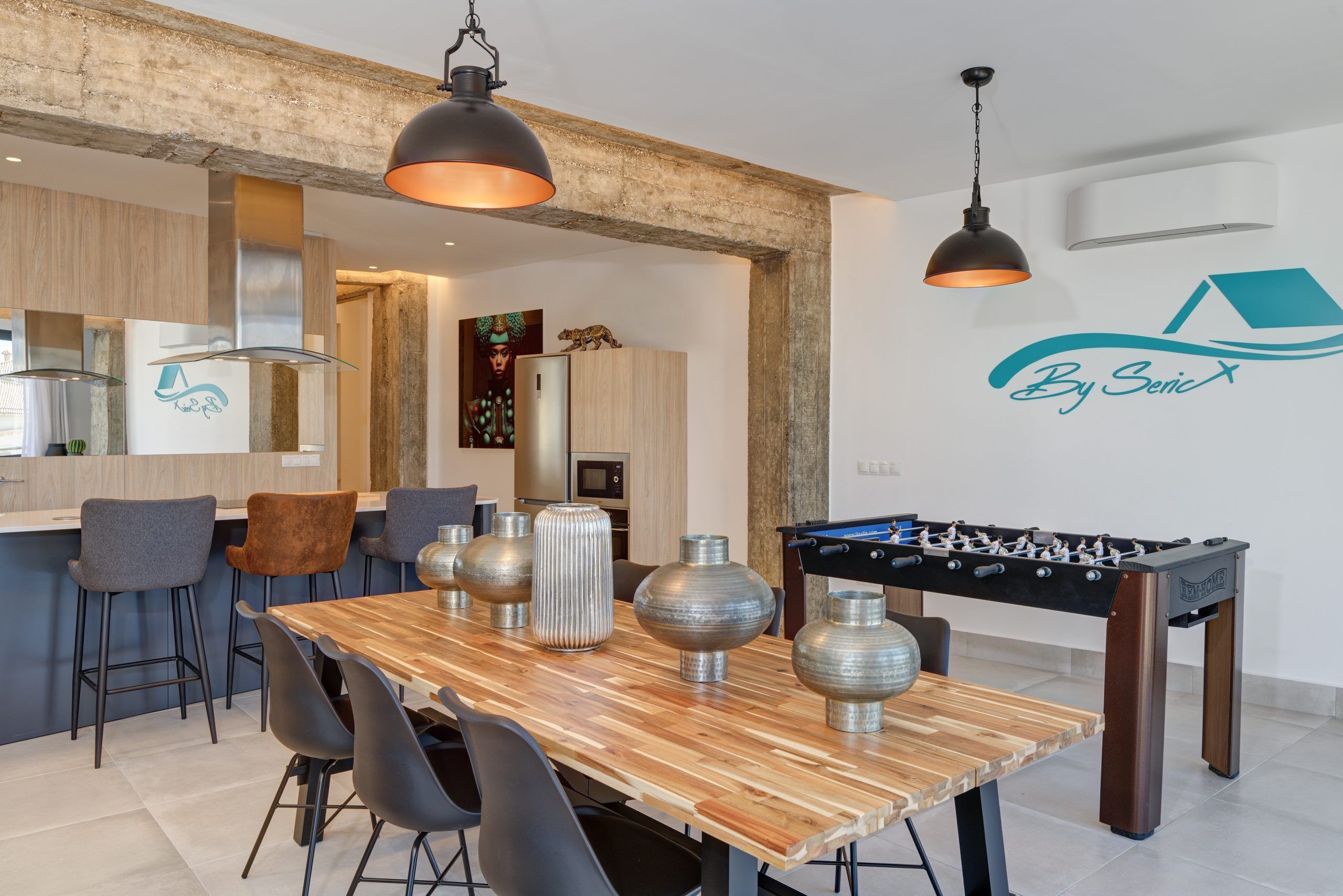 A modern kitchen with a wooden dining table, bar stools, and a foosball table.