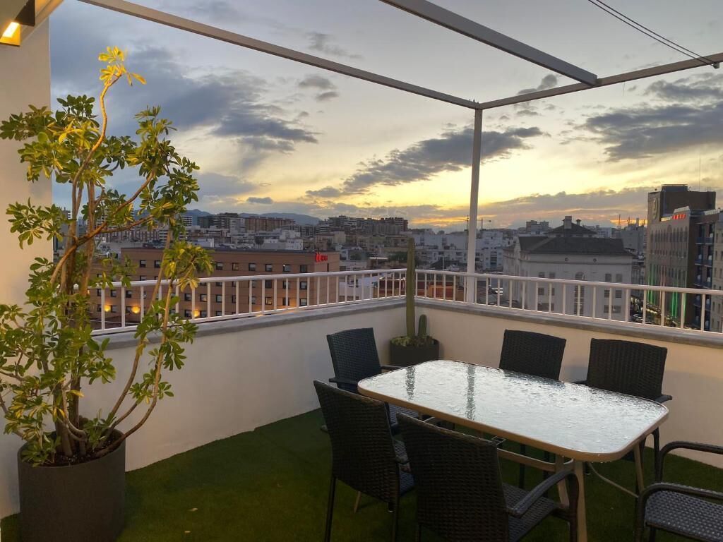 Ein Balkon mit Tisch und Stühlen, einer Topfpflanze und Blick auf die Stadt bei Sonnenuntergang.