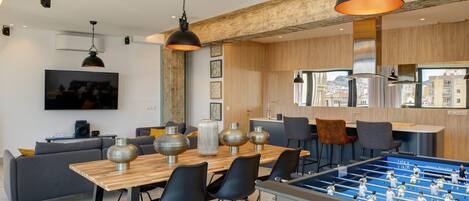 A modern living room with a foosball table, a wooden dining table, and a sofa.