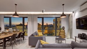Een moderne woonkamer met een eethoek, grote ramen met uitzicht op de stad en eigentijds meubilair.