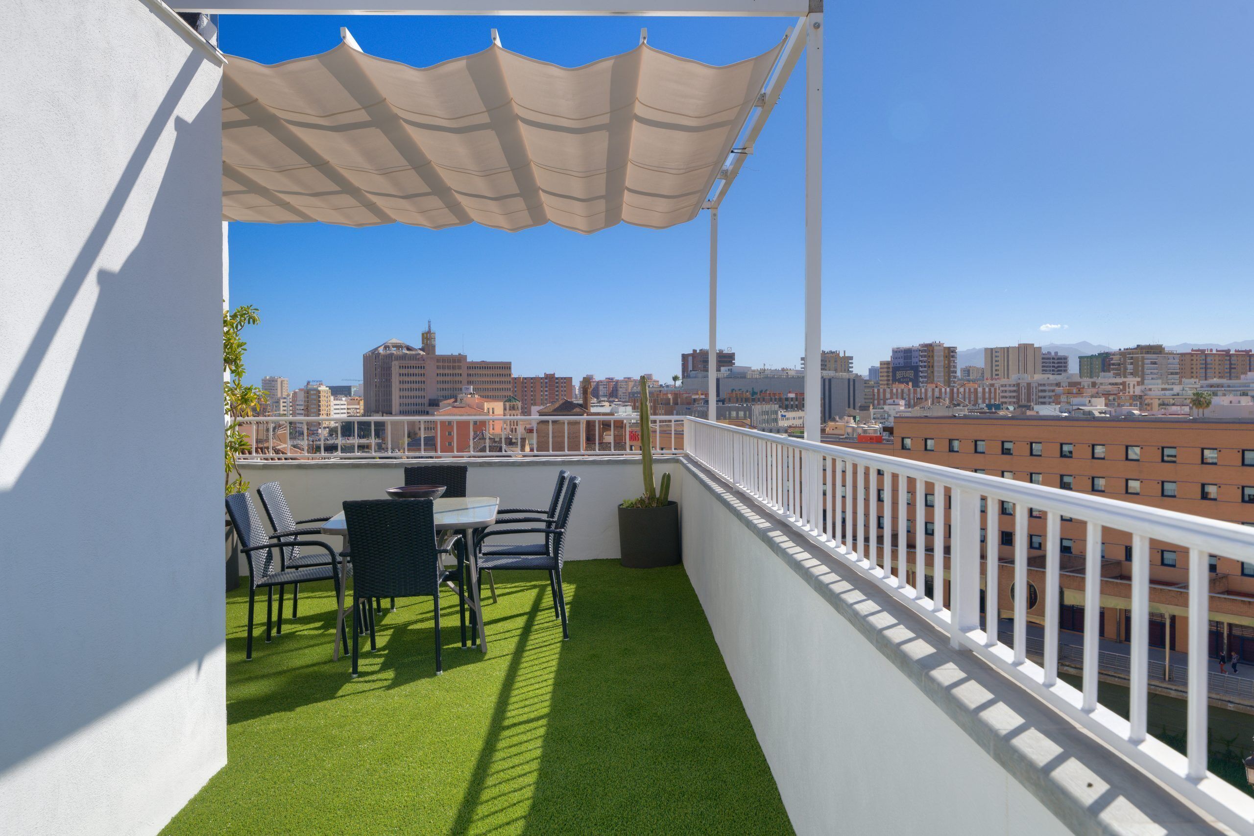 A balcony with artificial grass, a table, chairs, and a potted plant.