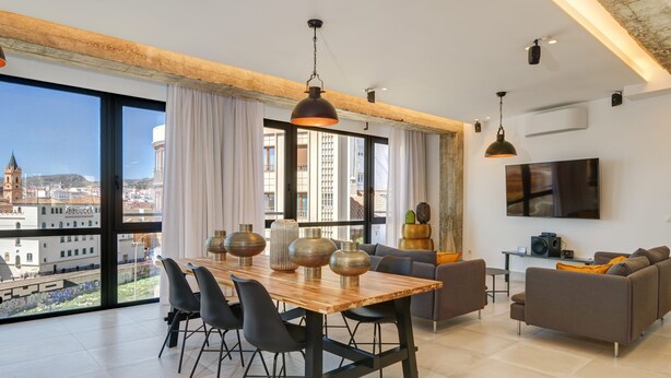Een ruime woonkamer met een grote eettafel, modern meubilair en een stadszicht door grote ramen.