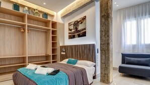 Een moderne slaapkamer met een grote inloopkast, een bed met een blauwgroene deken en een grijze bank.