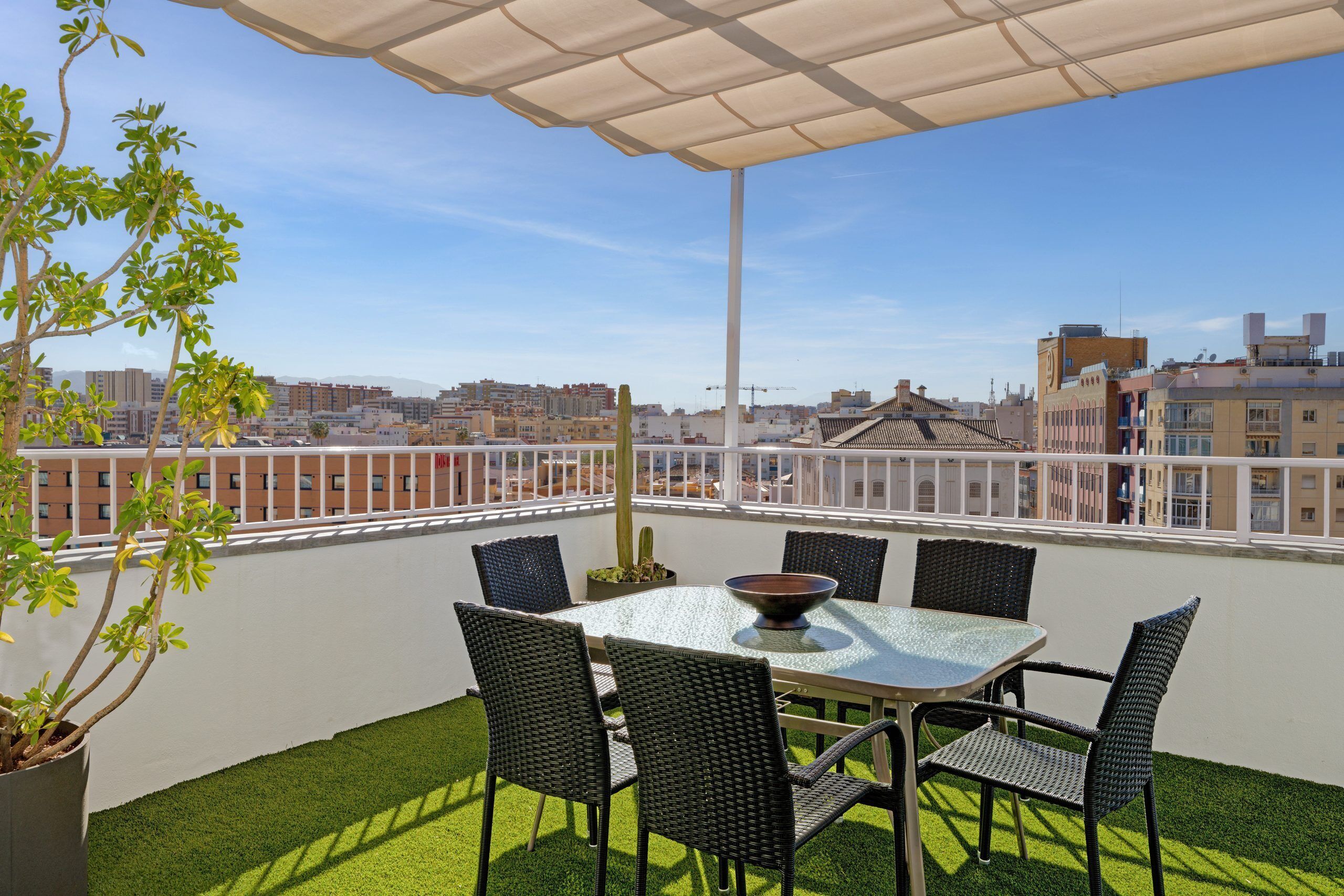 Una terraza en la azotea con mesa y sillas, una planta en maceta y vistas de la ciudad.