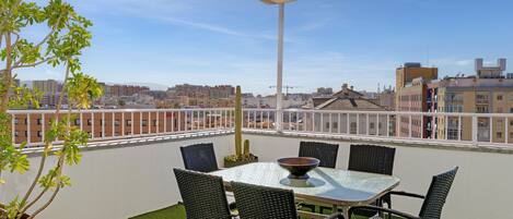 Una terraza en la azotea con mesa y sillas, una planta en maceta y vistas de la ciudad.