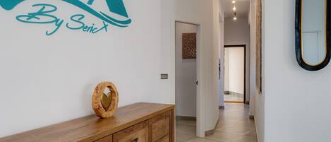 A hallway with a wooden cabinet, a wall-mounted mirror, and a sign reading "By SericX".