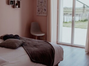 Ein Schlafzimmer mit Bett, Kissen, einem Sessel und einem großen Fenster.