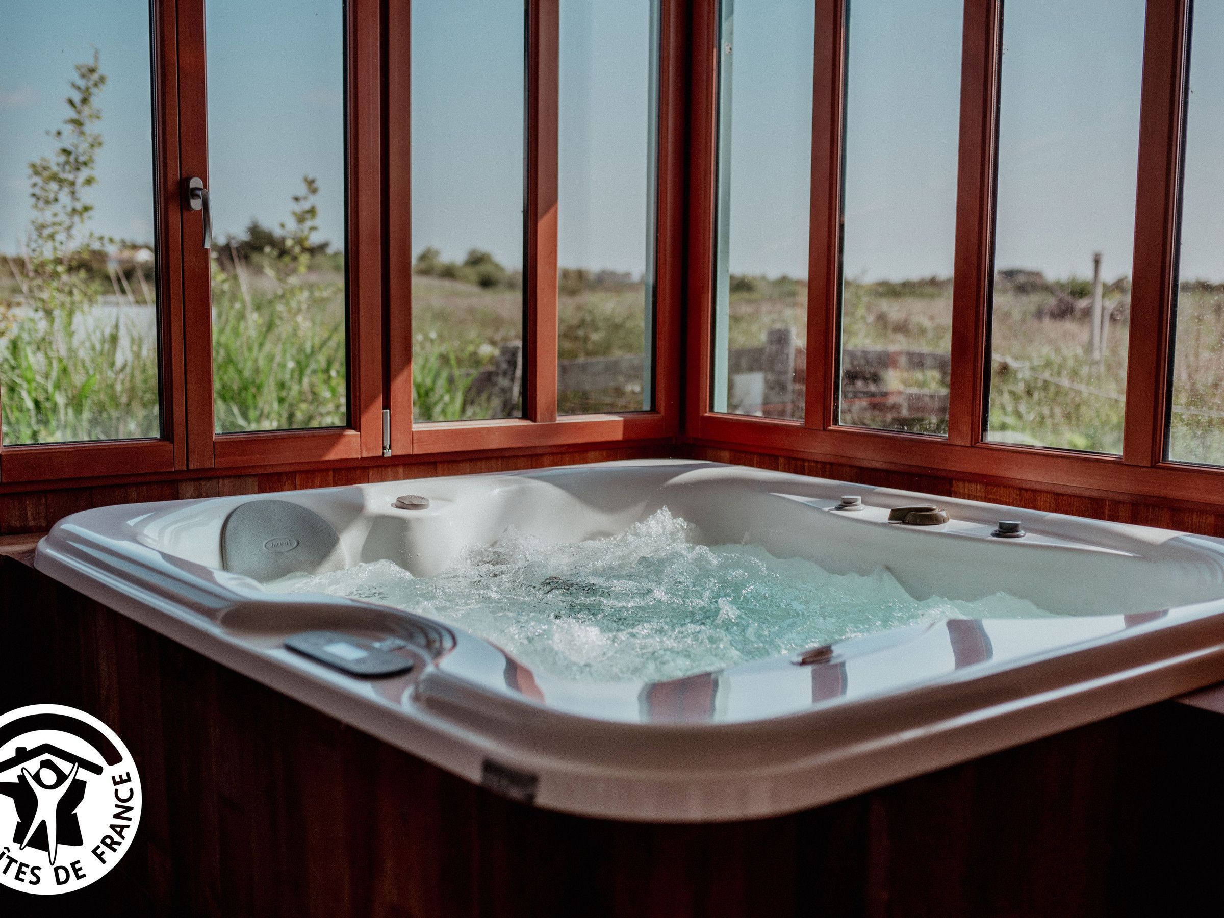 Un jacuzzi con vistas a un campo cubierto de hierba a través de amplios ventanales.