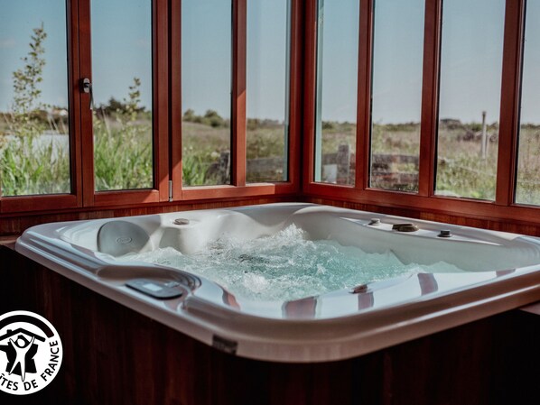 A hot tub with a view of a grassy field through large windows.