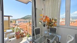 A balcony with a table and chairs, a vase with flowers, and a view of buildings and hills. - Casa Roma Apartment in Albenga (Albenga)